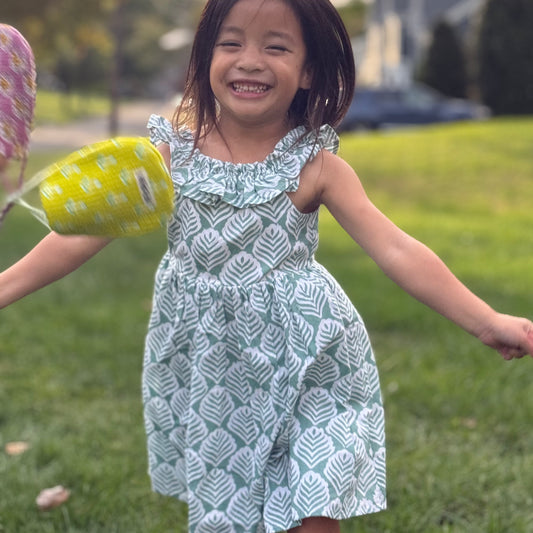 Girl happily jumping around wearing around cotton dress with leaf print