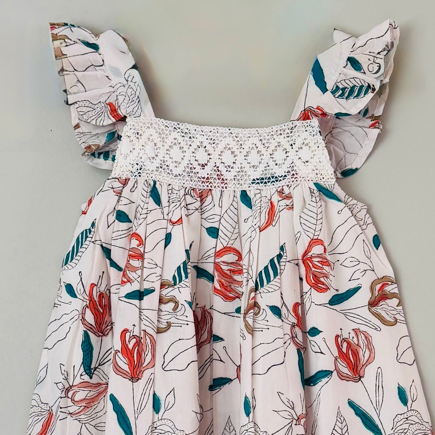 Close up of crochet lace yoke and coral floral block print detail on girls cotton summer dress soft breathable fabric