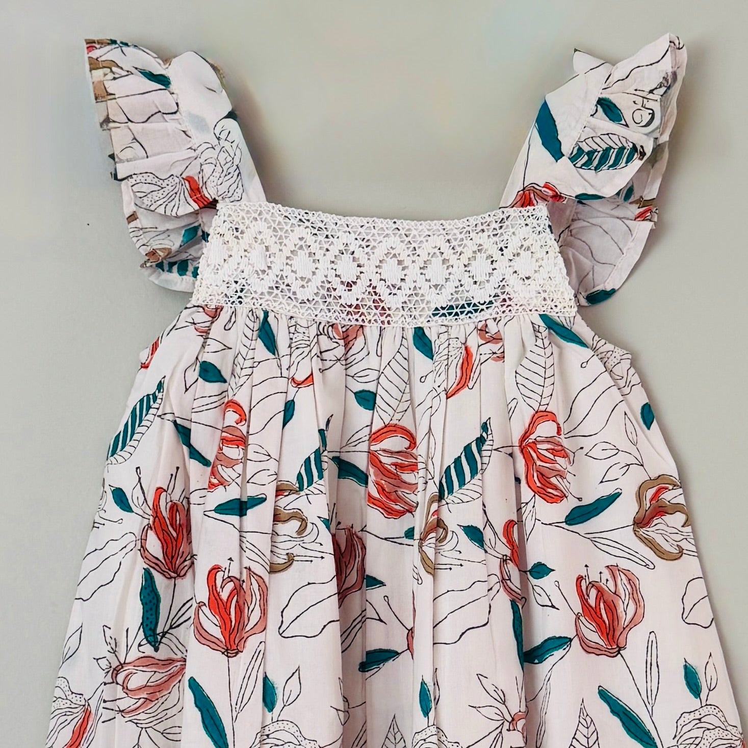 Close up of crochet lace yoke and coral floral block print detail on girls cotton summer dress soft breathable fabric