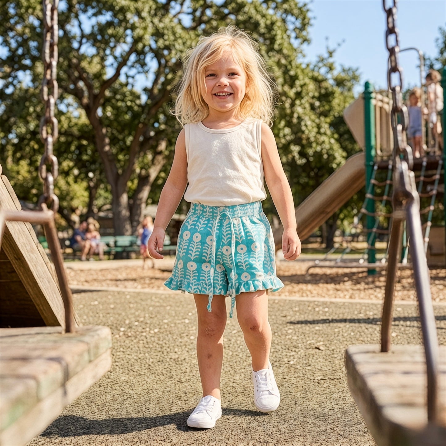 Young girl wearing teal floral cotton shorts with ruffle hem styled for summer outfit lightweight breathable playwear with White t-shirt